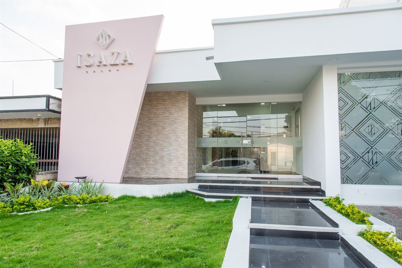 Fachada completa de Isaza Salón con su jardín y la entrada de vidrio con rombos